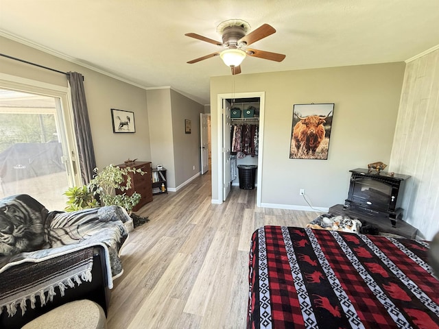 living room featuring wood finished floors, a wood stove, ceiling fan, baseboards, and ornamental molding
