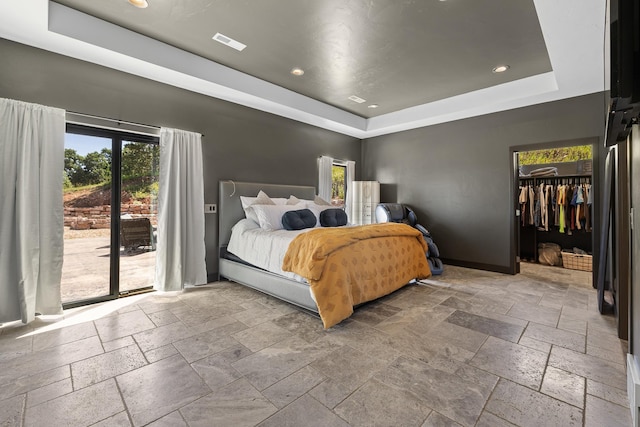 bedroom featuring a raised ceiling, stone tile flooring, recessed lighting, a walk in closet, and baseboards