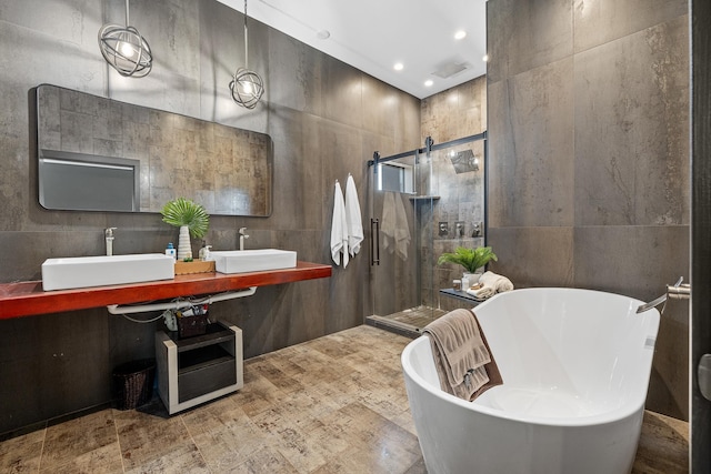 full bath with a sink, a stall shower, tile walls, a freestanding tub, and recessed lighting