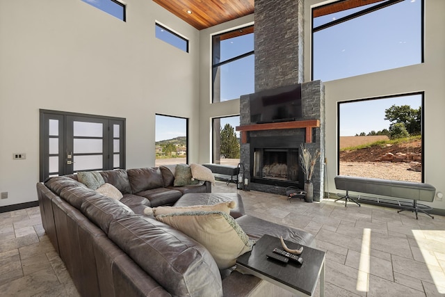 living area with stone tile floors, a high ceiling, wood ceiling, a stone fireplace, and baseboards