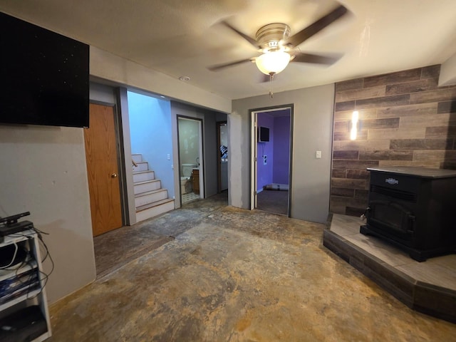 1304 River View Cir, Belle Fourche, SD 57717 - living area featuring a wood stove, wooden walls, ceiling fan, stairway, and concrete flooring