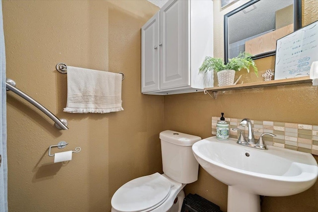 bathroom with a sink, toilet, and a textured wall
