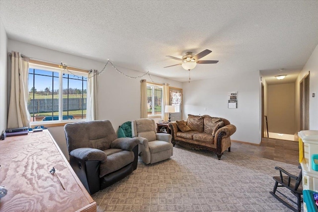 living area featuring ceiling fan, a textured ceiling, and baseboards