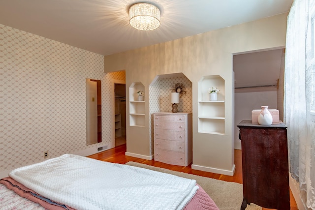 8510 Clarkson Rd, Rapid City, SD 57702 - bedroom with wood finished floors, a chandelier, wallpapered walls, a walk in closet, and baseboards