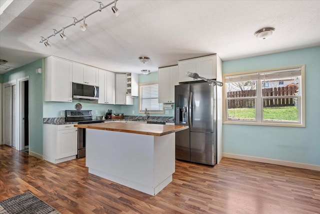 2921 1st Ave, Sturgis, SD 57785 - kitchen featuring butcher block countertops, appliances with stainless steel finishes, baseboards, rail lighting, and white cabinetry