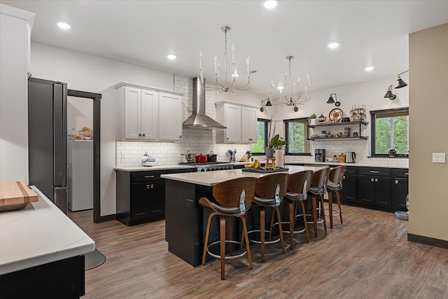 3135 American Eagle Rd, Spearfish, SD 57783 - kitchen featuring wall chimney range hood, wood finished floors, decorative backsplash, a kitchen island, and a breakfast bar area