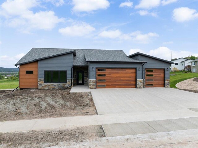 2431 Malibu Loop, Sturgis, SD 57785 - modern home featuring a garage, stone siding, concrete driveway, and a shingled roof