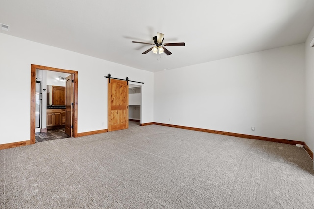 215 Meadowlark Dr, Hot Springs, SD 57747 - unfurnished bedroom featuring carpet, a barn door, a spacious closet, ensuite bath, and ceiling fan