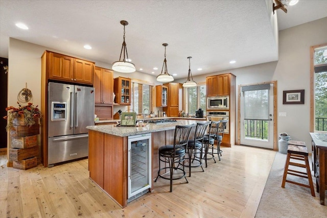 2040 Aster Rd, Spearfish, SD 57783 - kitchen featuring appliances with stainless steel finishes, wine cooler, brown cabinetry, light wood finished floors, and a breakfast bar
