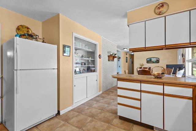 4103 W Main St, Rapid City, SD 57702 - kitchen with freestanding refrigerator, white cabinetry, light tile patterned floors, brick wall, and light countertops