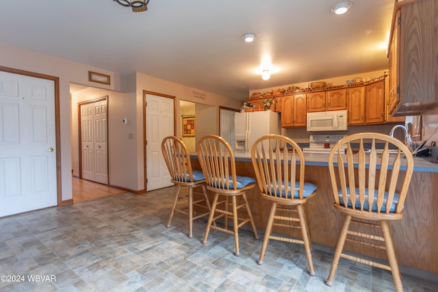 kitchen with a kitchen bar, white appliances, and kitchen peninsula