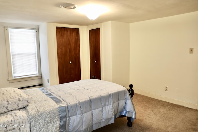 carpeted bedroom with a baseboard heating unit and two closets