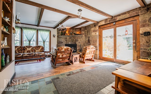 living room with beamed ceiling, hardwood / wood-style floors, and a stone fireplace