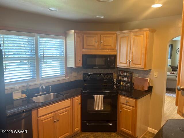 kitchen featuring black appliances, a sink, arched walkways, tasteful backsplash, and dark stone countertops