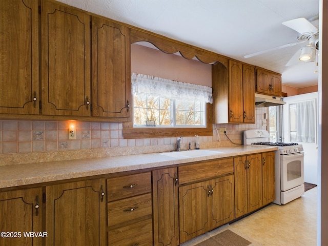 kitchen with ceiling fan, white range with gas stovetop, backsplash, and sink