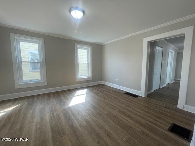 unfurnished room with visible vents, baseboards, ornamental molding, and dark wood-style flooring