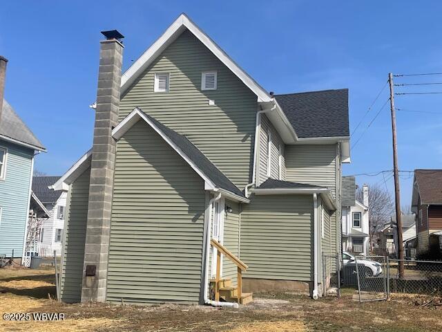 back of house with a shingled roof and fence