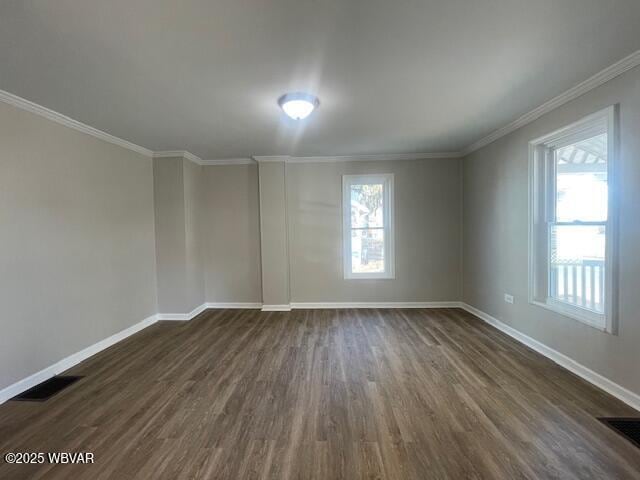 empty room featuring dark wood-style floors, visible vents, crown molding, and baseboards