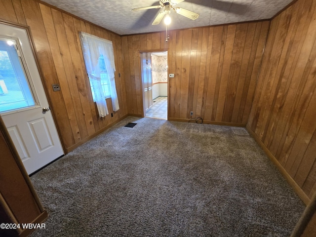 carpeted empty room with a textured ceiling, ceiling fan, and wooden walls