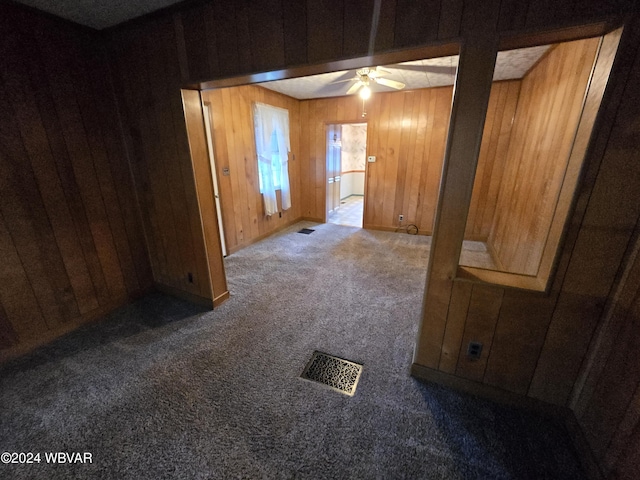 unfurnished room with wooden walls, carpet floors, and ceiling fan