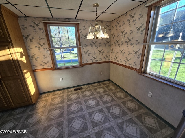 unfurnished dining area featuring dark parquet flooring, a drop ceiling, plenty of natural light, and a notable chandelier