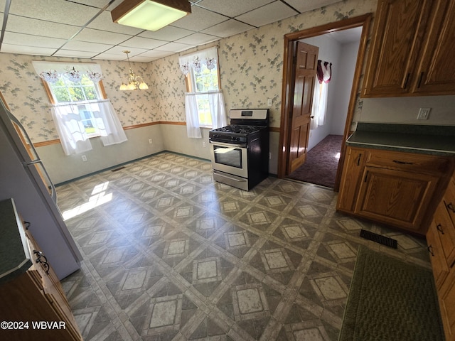 kitchen featuring pendant lighting, gas stove, fridge, and a paneled ceiling