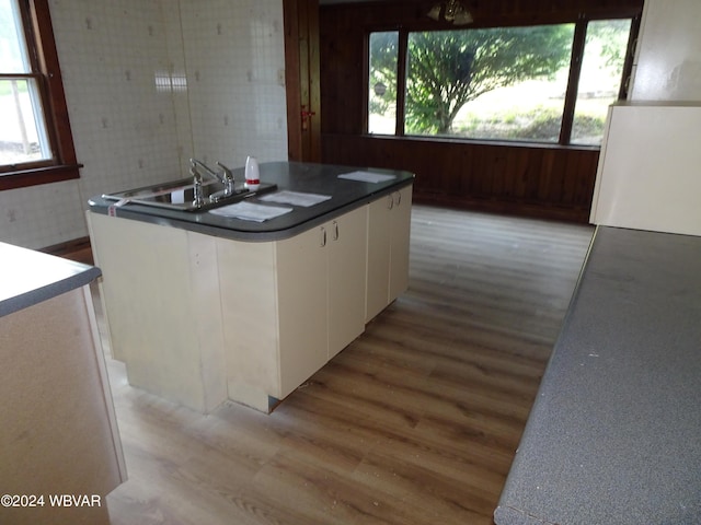 kitchen featuring white cabinets, wooden walls, light hardwood / wood-style floors, and a center island with sink