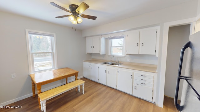 kitchen with white cabinetry, sink, black refrigerator, and light hardwood / wood-style flooring