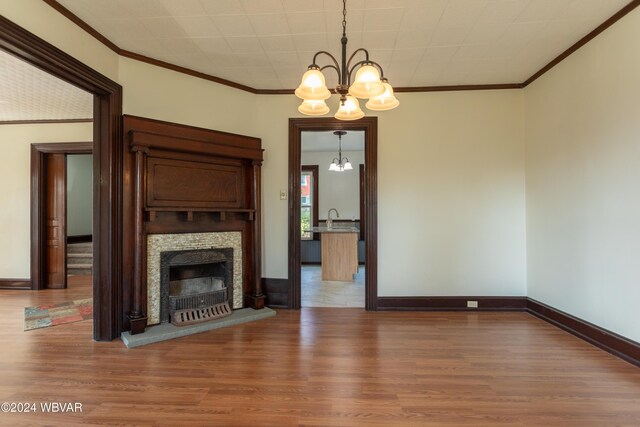 unfurnished living room with wood-type flooring, an inviting chandelier, crown molding, and sink