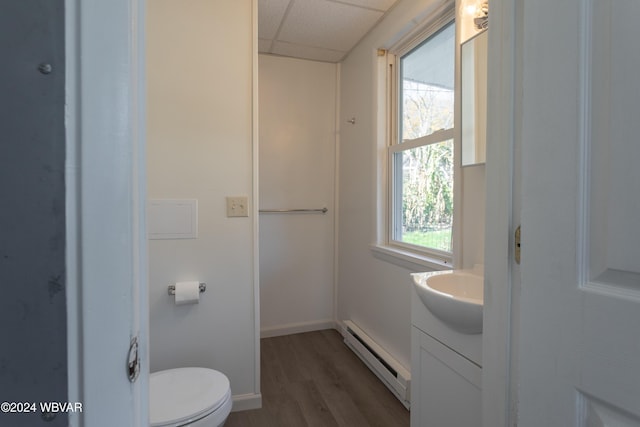 bathroom featuring a drop ceiling, wood-type flooring, plenty of natural light, and baseboard heating