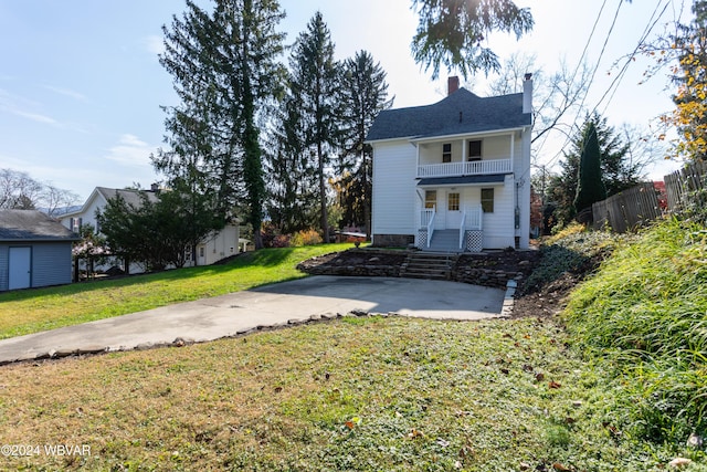 back of property featuring covered porch, a balcony, and a yard