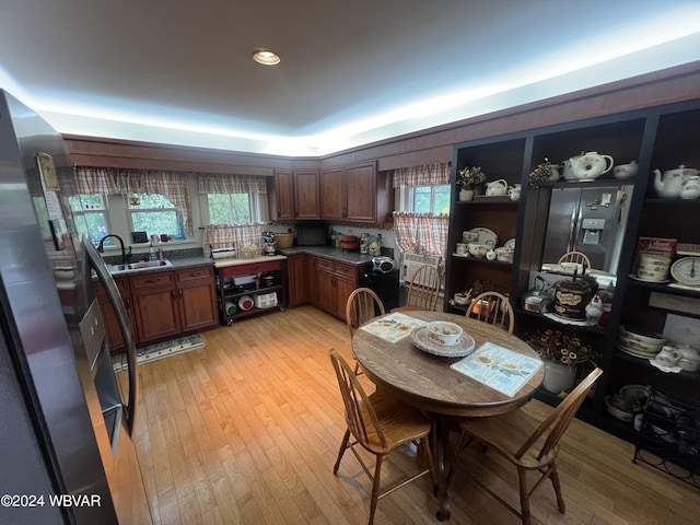 kitchen with sink, light hardwood / wood-style flooring, stainless steel refrigerator with ice dispenser, dark stone countertops, and stainless steel fridge