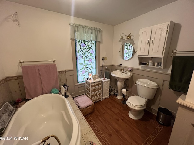 bathroom featuring a tub, sink, wood-type flooring, toilet, and tile walls