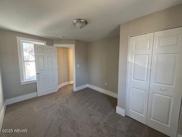 unfurnished bedroom featuring dark colored carpet, baseboards, and a closet