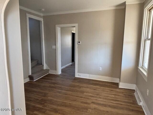 empty room featuring baseboards, dark wood finished floors, stairs, and ornamental molding