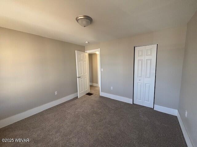 unfurnished bedroom with a closet, dark carpet, and baseboards