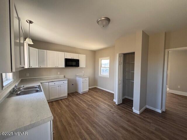 kitchen featuring baseboards, dark wood finished floors, a sink, black microwave, and white cabinetry