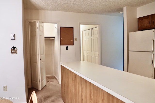 kitchen featuring white fridge, light colored carpet, and a textured ceiling