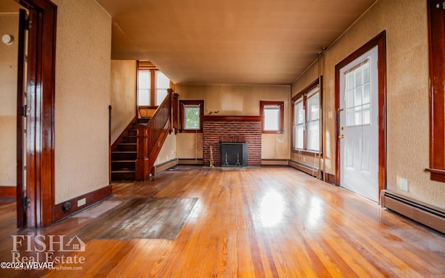 unfurnished living room featuring a brick fireplace, hardwood / wood-style floors, and a baseboard heating unit