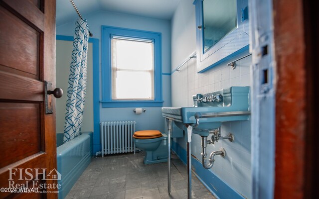 full bathroom featuring vaulted ceiling, sink, shower / bathtub combination with curtain, radiator heating unit, and toilet