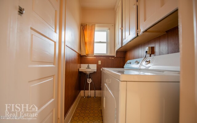 laundry area featuring wood walls, washer and clothes dryer, and cabinets