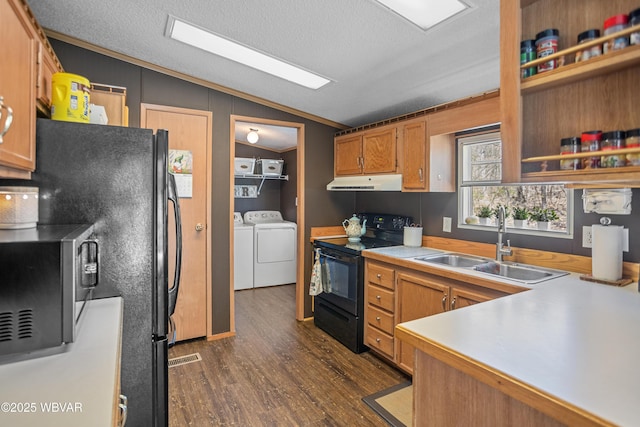 kitchen with a sink, under cabinet range hood, vaulted ceiling, washing machine and dryer, and black appliances