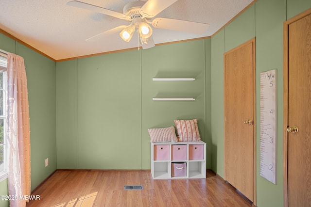 interior space featuring a textured ceiling, a ceiling fan, wood finished floors, and visible vents
