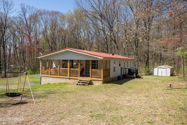 manufactured / mobile home featuring a porch, a shed, a front yard, a view of trees, and an outdoor structure