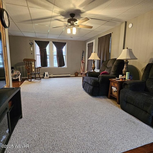 living room with baseboard heating, ceiling fan, a drop ceiling, and carpet