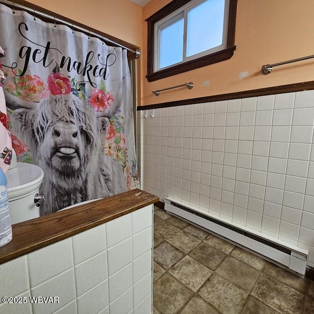 full bathroom featuring a baseboard heating unit, curtained shower, toilet, stone finish floor, and tile walls
