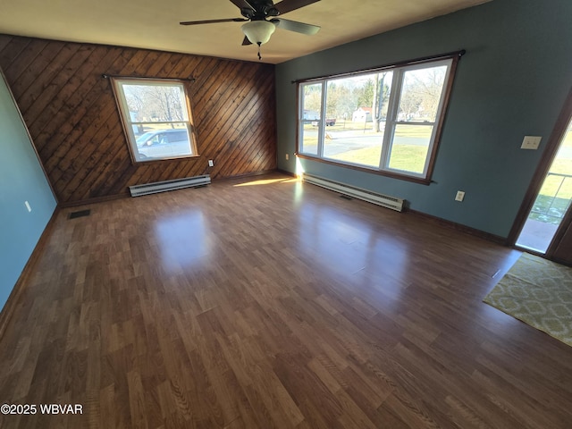 unfurnished living room with ceiling fan, a baseboard heating unit, dark hardwood / wood-style floors, and wood walls