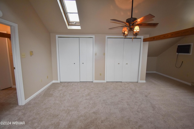 unfurnished bedroom featuring two closets, light colored carpet, lofted ceiling with skylight, and ceiling fan