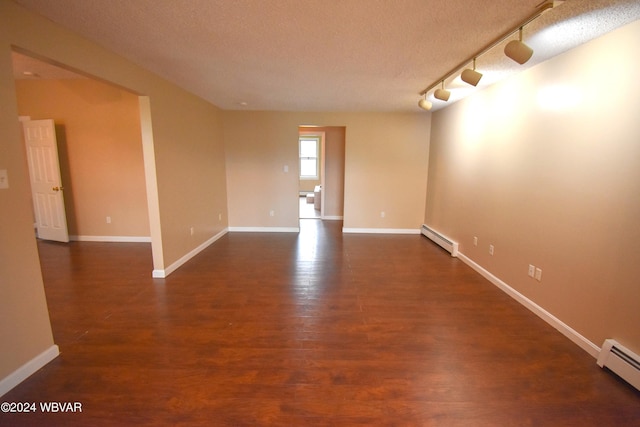 empty room with baseboard heating, rail lighting, and dark hardwood / wood-style floors