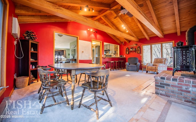 dining room featuring lofted ceiling with beams, a wood stove, wooden ceiling, and ceiling fan